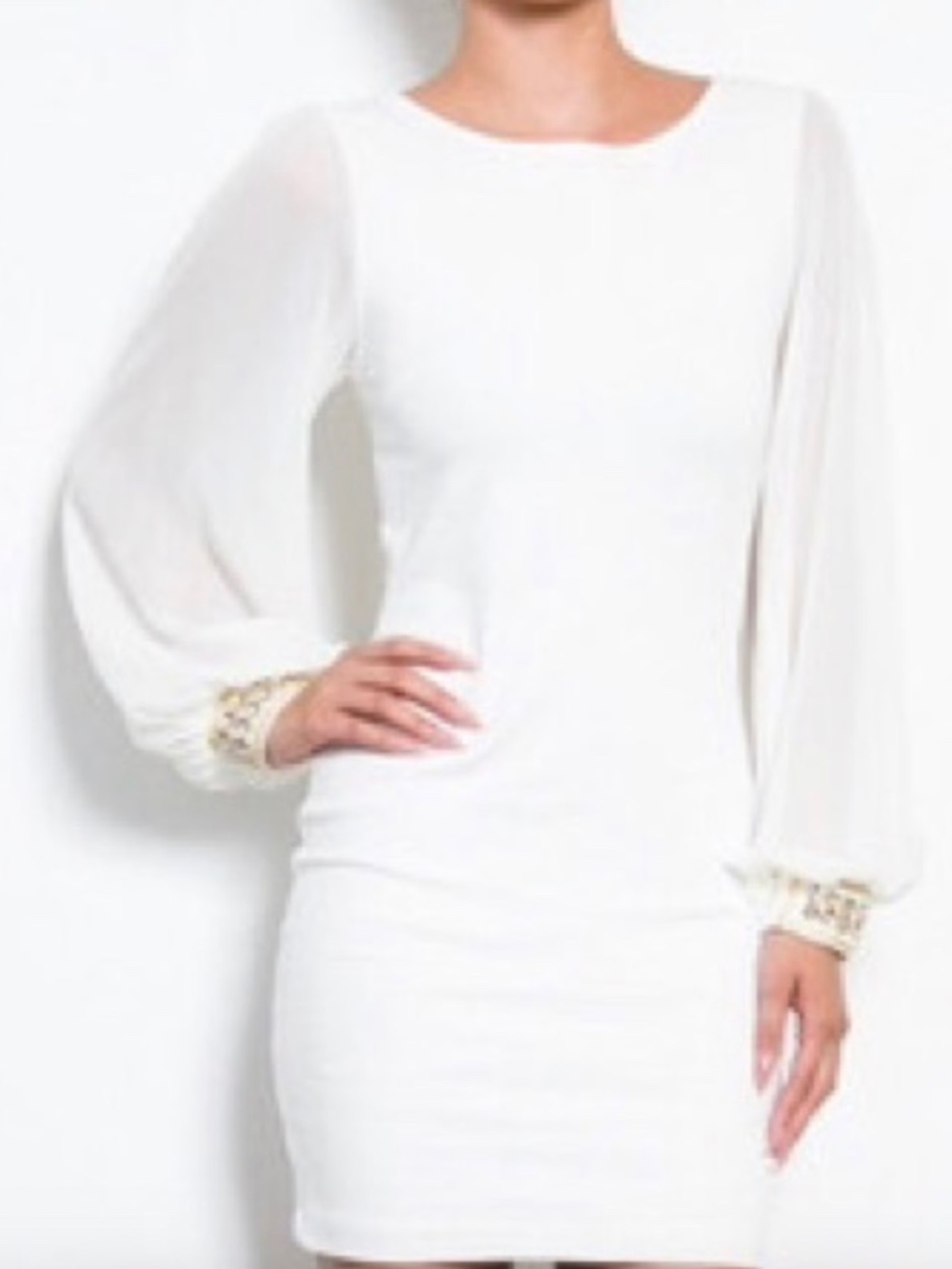 White dress above the knee with sheer sleeves and gold enhancements on wrist are